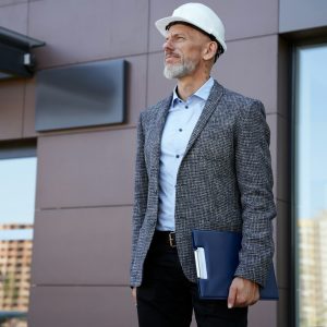 Monitoring the progress. Focused middle aged architect, engineer manager wearing helmet looking